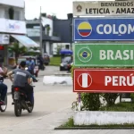 Fundo administrará US$ 10 bilhões para integração sul-americana foto mostra duas pessoas andando de moto pela rua, sem uso do capacete, uma ao lado da outra. Em primeiro plano, há uma placa de localização, com os nomes Colombia, Brasil e Peru. Esses países fazem parte da integração sul-americana
