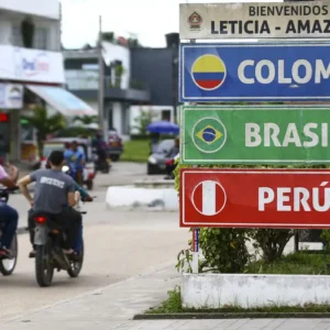 Fundo administrará US$ 10 bilhões para integração sul-americana foto mostra duas pessoas andando de moto pela rua, sem uso do capacete, uma ao lado da outra. Em primeiro plano, há uma placa de localização, com os nomes Colombia, Brasil e Peru. Esses países fazem parte da integração sul-americana