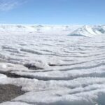 Dois pesquisadores em trajes de proteção em uma paisagem de gelo na Antártida.
