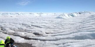 Dois pesquisadores em trajes de proteção em uma paisagem de gelo na Antártida.