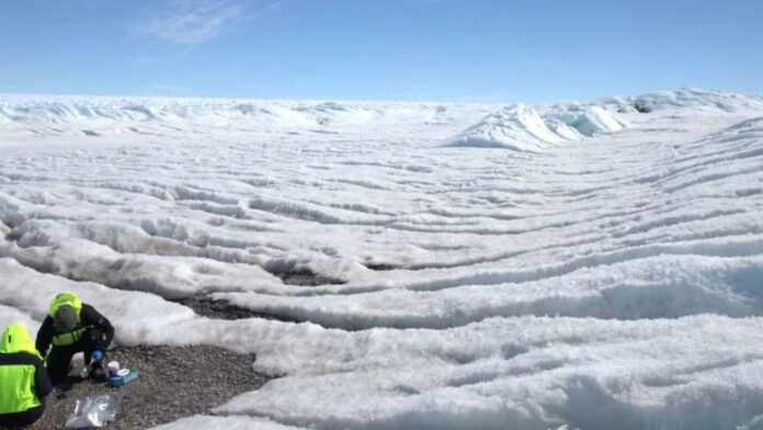 Dois pesquisadores em trajes de proteção em uma paisagem de gelo na Antártida.