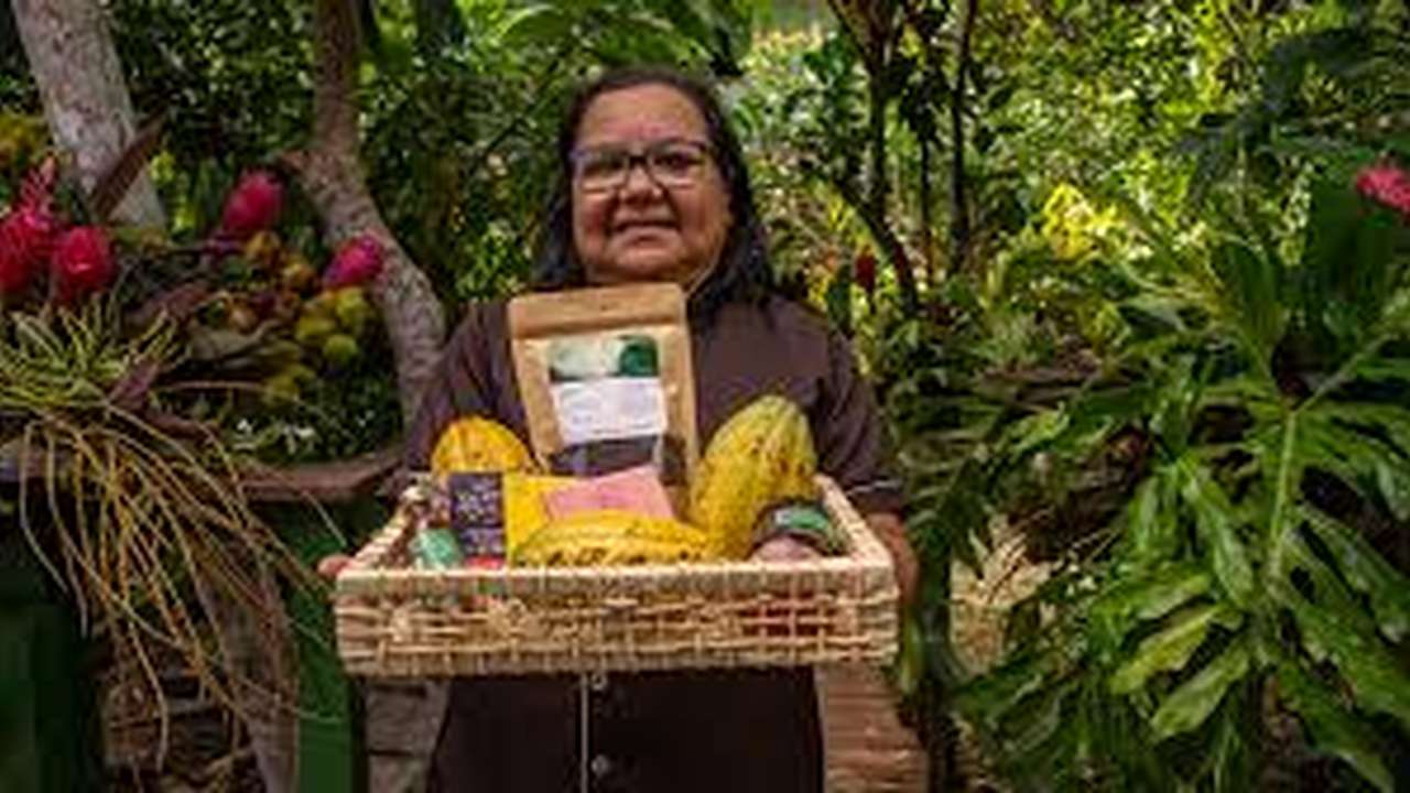 Dona Nena, em sua fábrica de chocolates no Combu, segura uma cesta cheia de ingredientes como cacau e frutas.