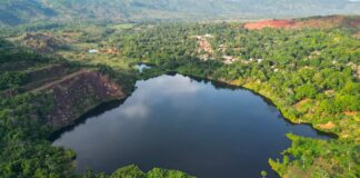 Lago azul profundo cercado por vegetação verde em Serra Pelada, com uma vila no topo da colina ao fundo