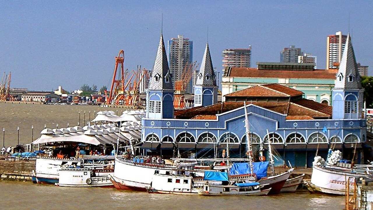 Mercado de peixe em Belém, Pará, Brasil, com barcos coloridos atracados na beira do rio, edifícios históricos e um céu azul claro.