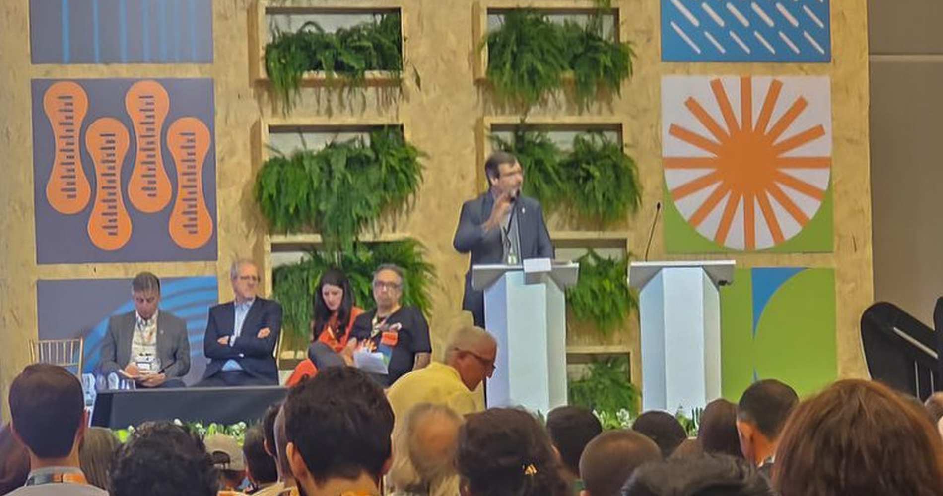 Palestrante falando em um evento sobre governança global e educação ambiental, com público presente.