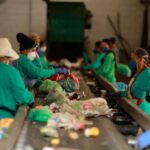 A virada verde do Brasil: Decreto federal obriga uso de plástico reciclado em embalagens Trabalhadores em uma linha de montagem de reciclagem, usando máscaras e luvas, classificam e separam lixo reciclável.