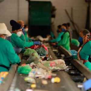 A virada verde do Brasil: Decreto federal obriga uso de plástico reciclado em embalagens Trabalhadores em uma linha de montagem de reciclagem, usando máscaras e luvas, classificam e separam lixo reciclável.