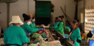 Trabalhadores em uma linha de montagem de reciclagem, usando máscaras e luvas, classificam e separam lixo reciclável.