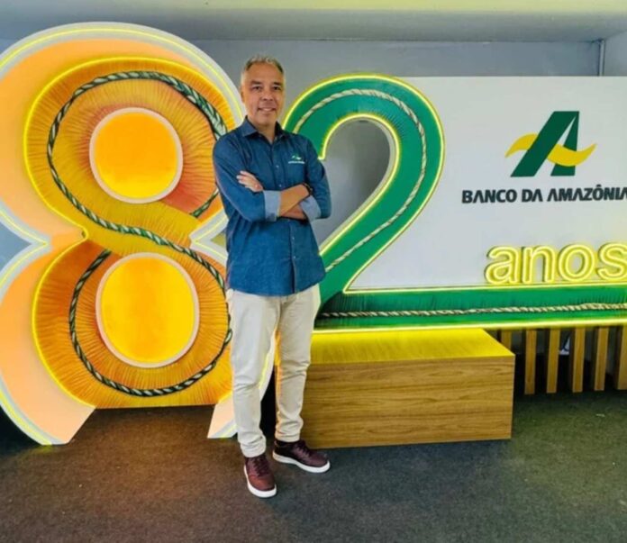 Um homem em camisa azul e calca bege sorri e posa em frente a um letreiro do banco da amazonia que celebra 82 anos com um fundo de madeira 20250512171230 Banco da Amazônia promove bioeconomia na Agrobalsas 2025