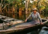 Como o gigante pirarucu e o manejo comunitário revolucionam a economia sustentável nos lagos do Amazonas Fotografia documental na luz da tarde de um pescador ribeirinho em canoa com pirarucu recém-pescado em lago de igapó floresta inundada ao fundo.