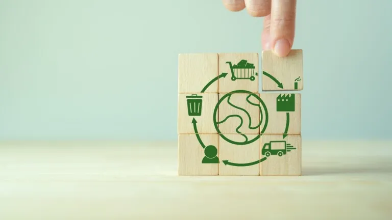 Produção de insumos virgens cresce e ameaça avanço da economia circular 2 Blocos de madeira com ícones que representam a circularidade de um produto, como produção, consumo, descarte e reutilização, com a mão posicionando o bloco que representa a etapa de descarte