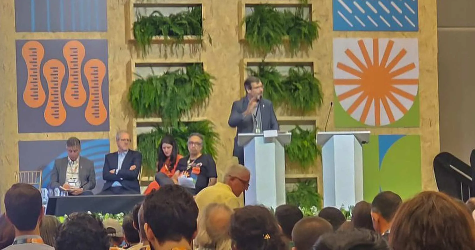 Palestrante falando em um evento sobre governança global e educação ambiental, com público presente.