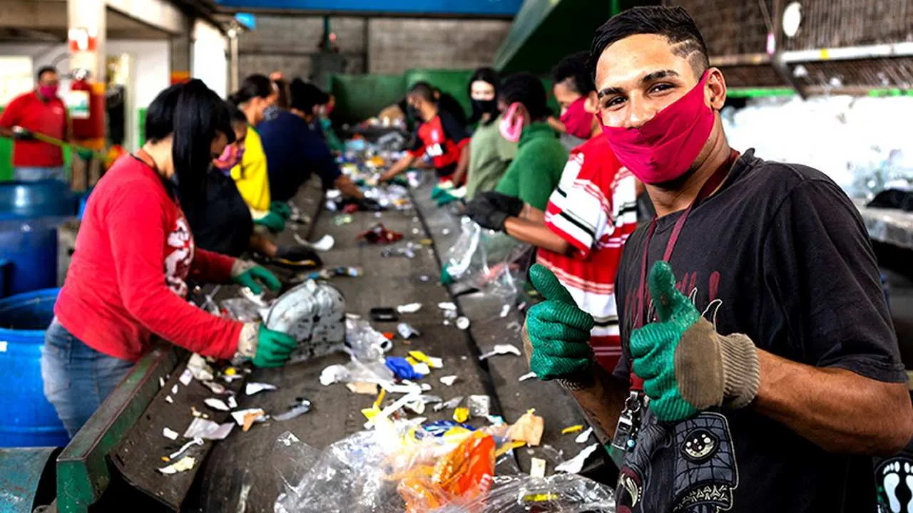 trabalhadores-em-uma-linha-de-reciclagem-selecionando-e-separando-o-lixo-um-homem-sorri-e-mostra-o-polegar-para-cima-usando-luvas-verdes-e-uma-mascara-facial-20250521000435 Governo revoga decreto de importação de resíduos recicláveis após mobilização de catadores