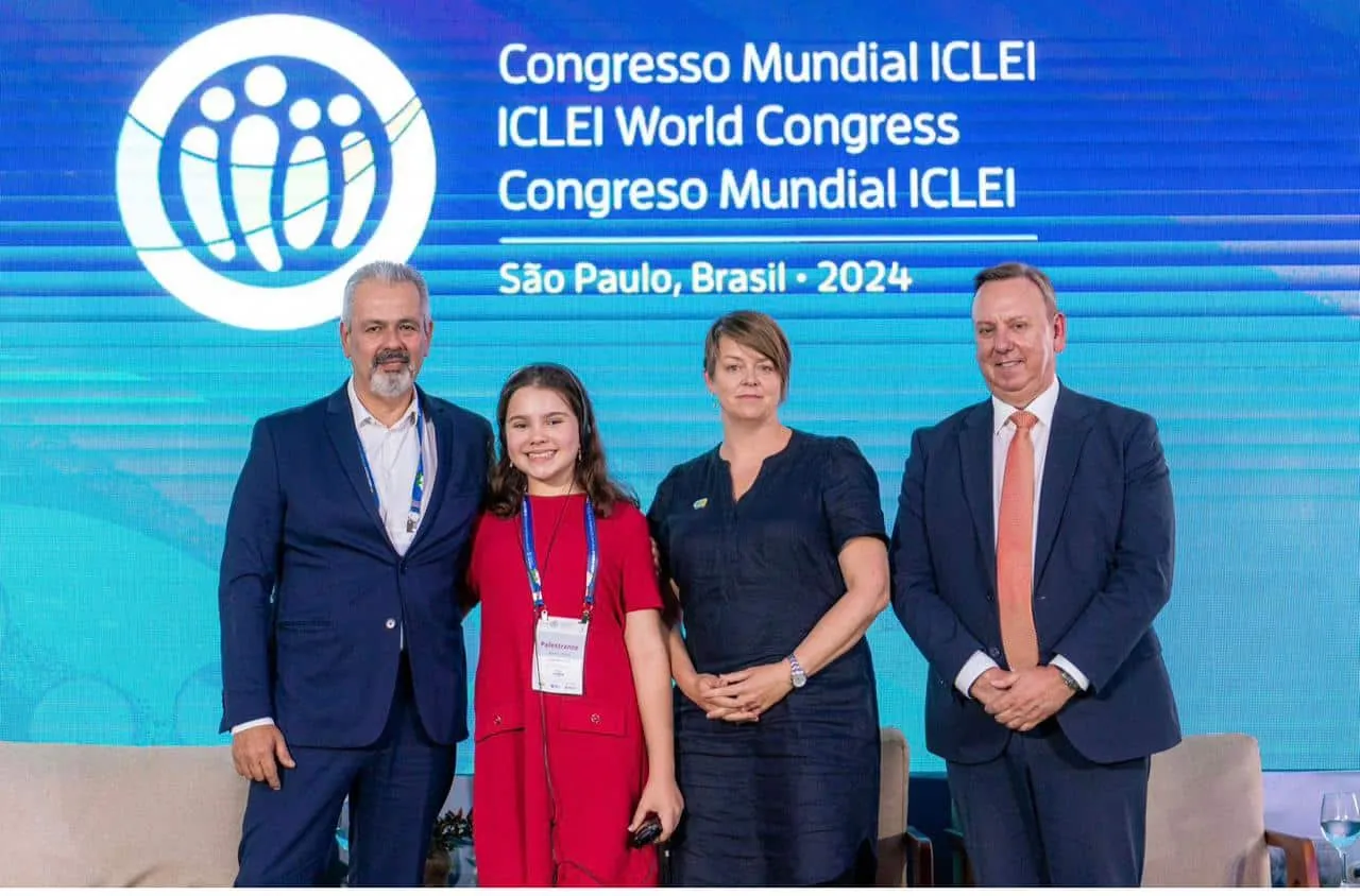 A estudante mineira Júlia Bonitese, de apenas 13 anos, foi convidada oficialmente a participar da COP-30, a Conferência das Nações Unidas sobre Mudanças Climáticas, que será realizada em Belém (PA). Júlia participará do painel “Diálogo Intergeracional de Alto Nível sobre Crianças e Clima”, dia 17 de novembro, dentro da Zona Azul, área reservada a embaixadores, autoridades e líderes globais — o que faz de sua presença um marco histórico para a representatividade infantojuvenil brasileira no debate climático internacional. Fundadora do projeto Pequenos Protetores do Planeta (@projeto.ppp), Júlia atua desde os 8 anos como ativista ambiental e defensora dos direitos de crianças e adolescentes na agenda climática. É Embaixadora da Justiça Climática pela Plant-for-the-Planet Brasil, consultora da organização internacional Child Rights Connect, ligada à ONU, e membro da Rede Primeira Infância de Minas Gerais. Em seu projeto, ela promove ações presenciais de educação ambiental, como palestras, plantios e campanhas, além de conduzir o programa “Papo Natural”, em que entrevista especialistas no YouTube sobre temas como preservação, sustentabilidade e participação cidadã. Júlia também é presença constante em fóruns e câmaras legislativas, defendendo o direito de voz das crianças. Dentre essas participações, atuou na elaboração e apresentação da “Declaração das Juventudes de Belo Horizonte pelo Clima” na Câmara Municipal, junto à LCOY, e compôs a mesa de debates no evento nacional “Crianças e Jovens Rumo à COP-30”, em Brasília. Reconhecida como uma das principais vozes da juventude ambiental no país, Júlia já recebeu dois prêmios nacionais e um internacional: foi a primeira criança agraciada com o Prêmio Hugo Werneck de Sustentabilidade, o mais importante do Brasil na área, e recebeu o título de Embaixadora Regional da América Latina e Caribe pela Plant-for-the-Planet Global. Em 2024, representou o Brasil no ICLEI World Congress, onde encerrou o evento diante de centenas de líderes políticos mundiais. Na COP-30, Júlia apresentará uma fala voltada à educação ambiental, à redução das desigualdades e à responsabilidade compartilhada entre governos, empresas e cidadãos. Sua mensagem principal destaca o protagonismo das crianças e jovens como agentes de mudança, não apenas vítimas da crise climática. “Meu sonho é que as decisões sobre o clima também considerem a voz das crianças. Somos nós que viveremos as consequências do que está sendo decidido agora”, diz Júlia. A escola tem papel central na rotina e na visão de mundo de Júlia que, além de se dedicar prioritariamente aos estudos, vê na educação ambiental parte essencial da formação de crianças e adolescentes. Para ela, é por meio da escola que o conhecimento se transforma em consciência e ação. Ao conciliar os estudos com projetos e eventos socioambientais, demonstra que aprender e agir podem caminhar juntos, sem abrir mão das experiências próprias da infância. Mesmo reconhecida por sua atuação em projetos e eventos de relevância global, Júlia diz que o projeto deve ser de muitos, e ressalta que gostaria muito de expandi-lo a mais crianças e jovens e a mais territórios pois, para ela, ampliar o acesso ao conhecimento é o caminho para transformar o mundo. “É preciso conhecer para desejar proteger — esse é o lema do meu projeto. E por isso eu desejo chegar a mais e mais crianças e jovens a cada dia, para que eles tenham a chance de conhecer os problemas climáticos e se identificarem como solução. Juntos somos força!”, afirma. Com atividades desenvolvidas de forma independente e sem apoio corporativo, Júlia sente por não conseguir expandir suas ações presenciais e também o programa Papo Natural. “Tudo tem um custo e nem sempre dá pra fazer tudo o que eu planejo. O Papo Natural está parado por causa dos gastos com estúdio e edição, mas o projeto tem muito potencial. Nele eu dou voz a outras crianças e levo conhecimento sem fronteiras. É só entrar no YouTube”, explica.